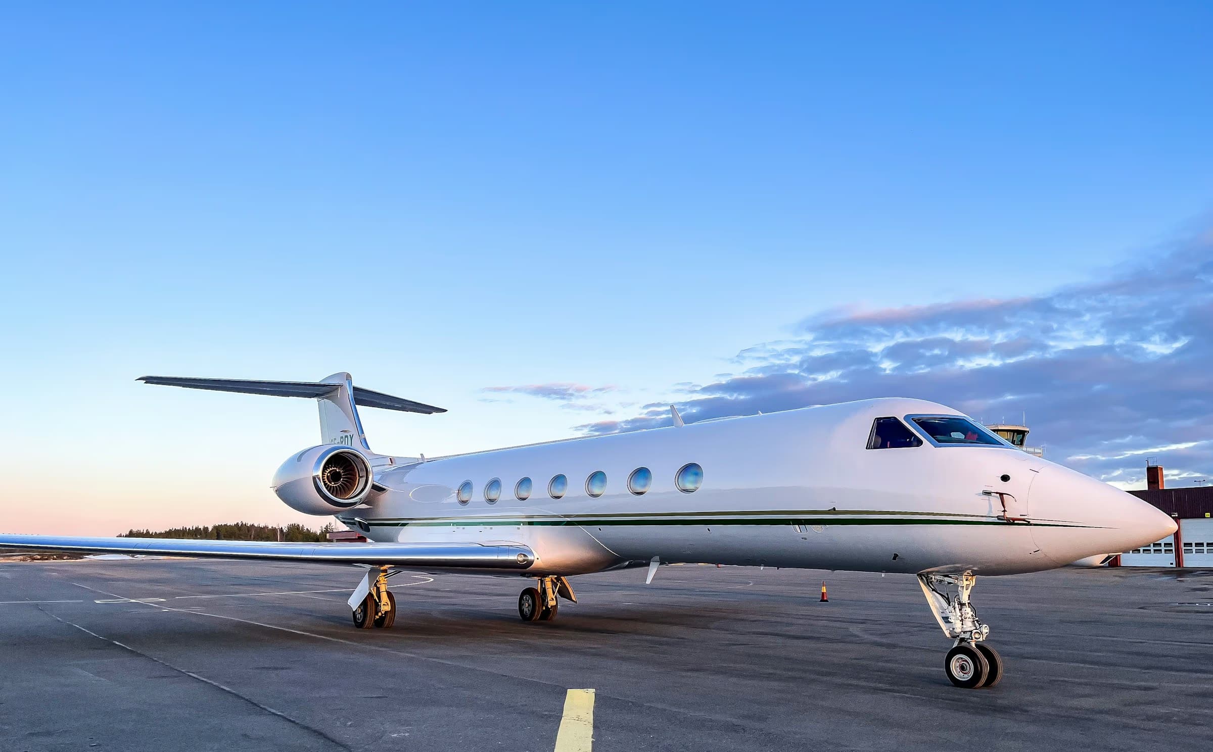 A Gulfstream heavy jet at rest on an open apron at dusk, nose toward the camera, sky clearing behind
